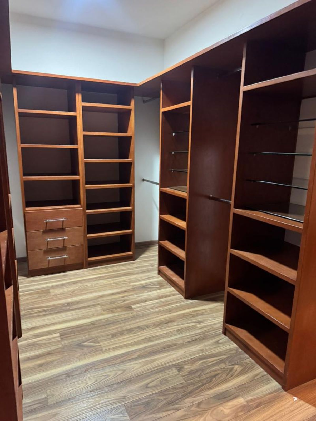 Vestidor con muebles de madera oscura, múltiples estantes, cajones y piso de madera laminada