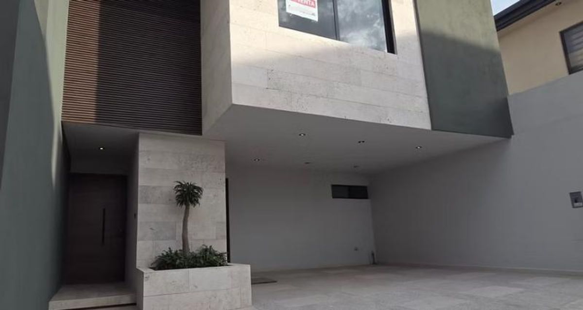 Fachada moderna con cochera techada, revestimiento de piedra clara, puerta oscura y pequeña jardinera
