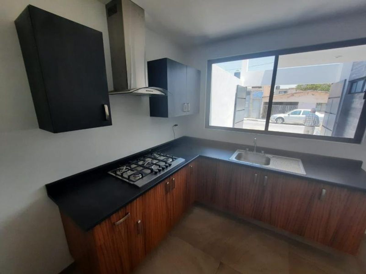 Cocina integral con gabinetes de madera, cubierta negra, campana de acero inoxidable y ventanal