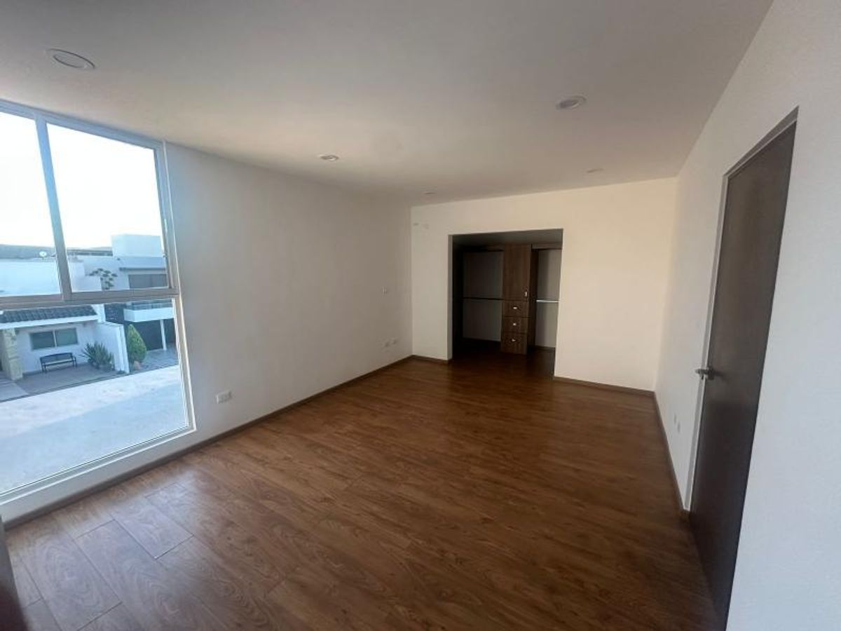 Habitación vacía con piso de madera, ventana grande, paredes blancas y vestidor de madera