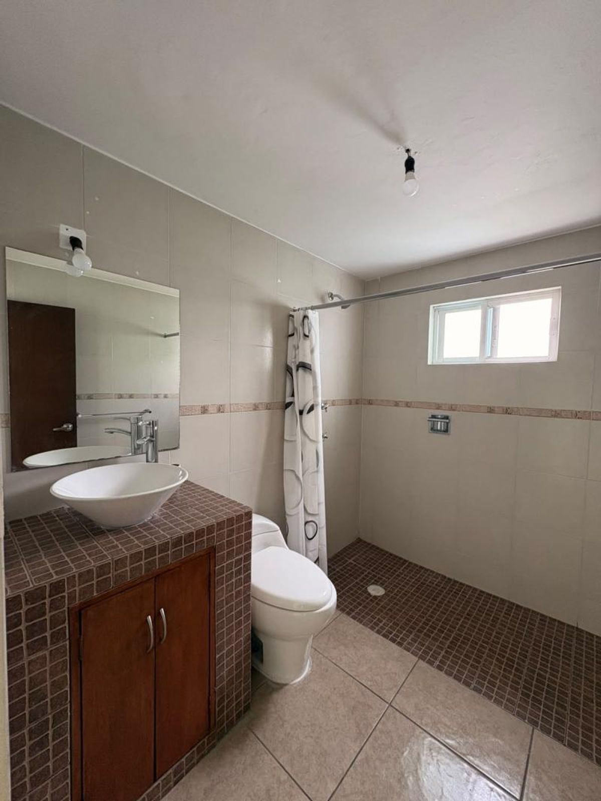 Baño con lavabo tipo tazón en mueble de mosaico, sanitario blanco y regadera