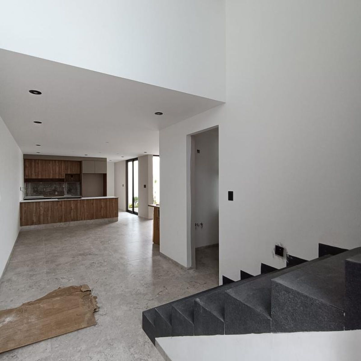Espacio abierto con piso gris claro, cocina con gabinetes de madera y escalera negra