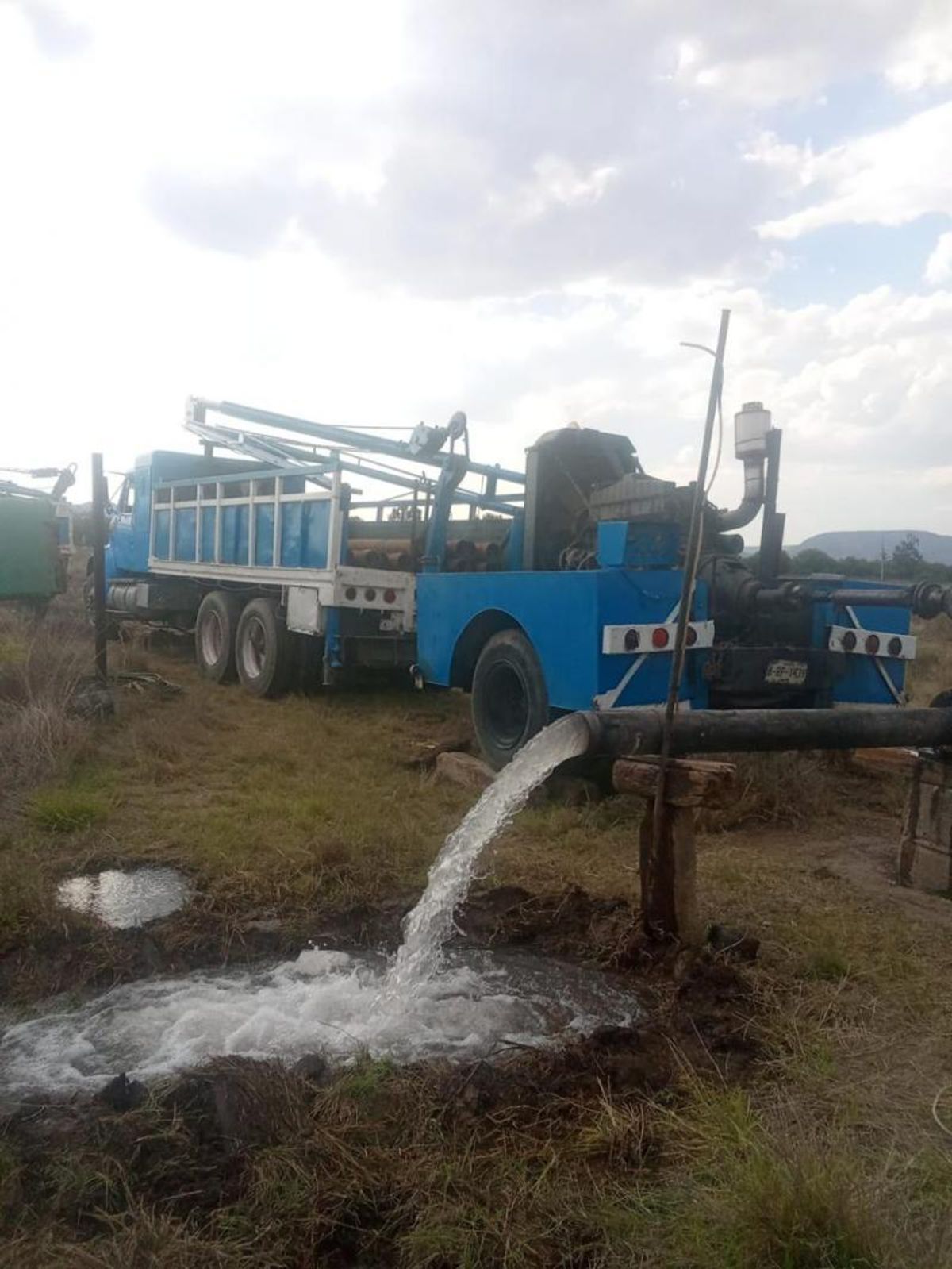 Camión con equipo de pozo bombeando abundante agua por tubería hacia el terreno