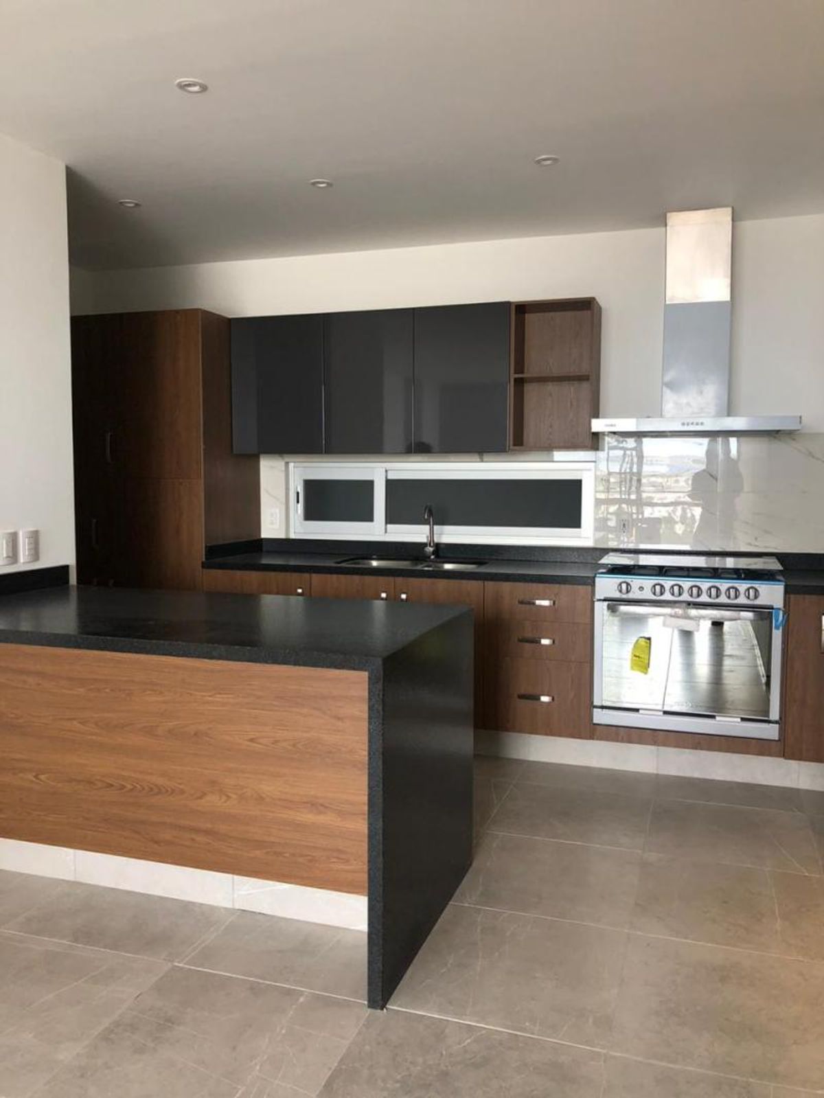 Cocina integral con isla de cubierta negra, gabinetes de madera y estufa de acero inoxidable
