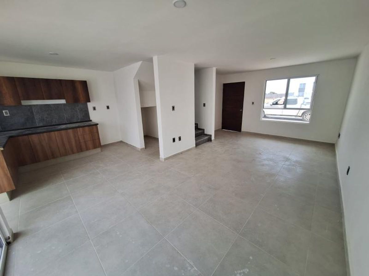 Espacio abierto con cocina integral de madera, piso cerámico gris, escaleras y puerta principal