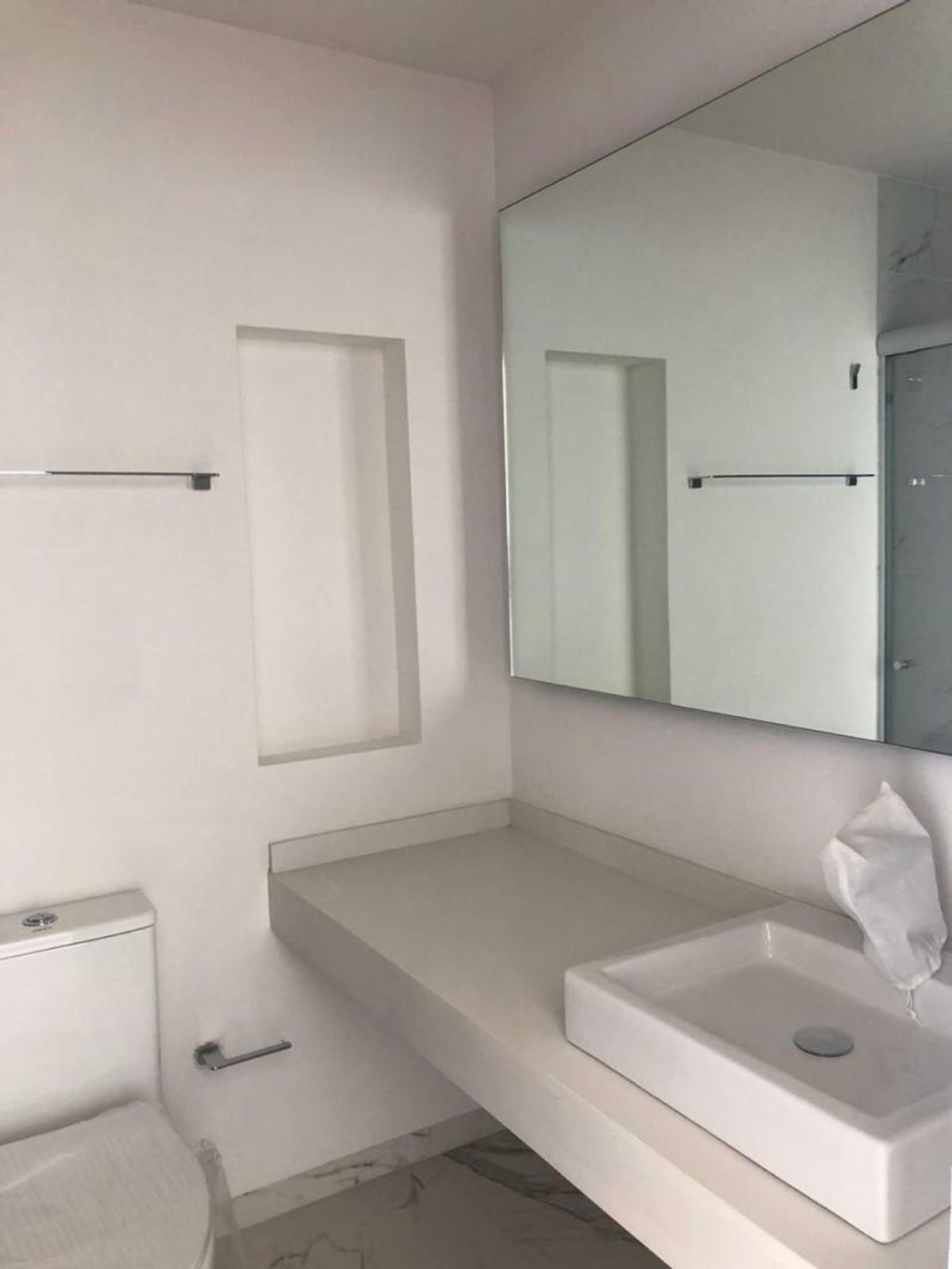 Baño con lavabo rectangular sobre cubierta clara, espejo amplio, sanitario y nicho en pared