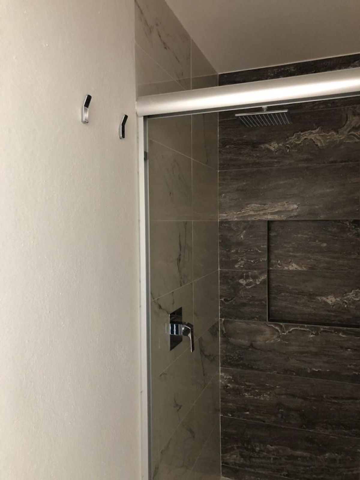 Regadera con revestimiento de azulejo tipo mármol oscuro cancel de cristal y grifería cromada