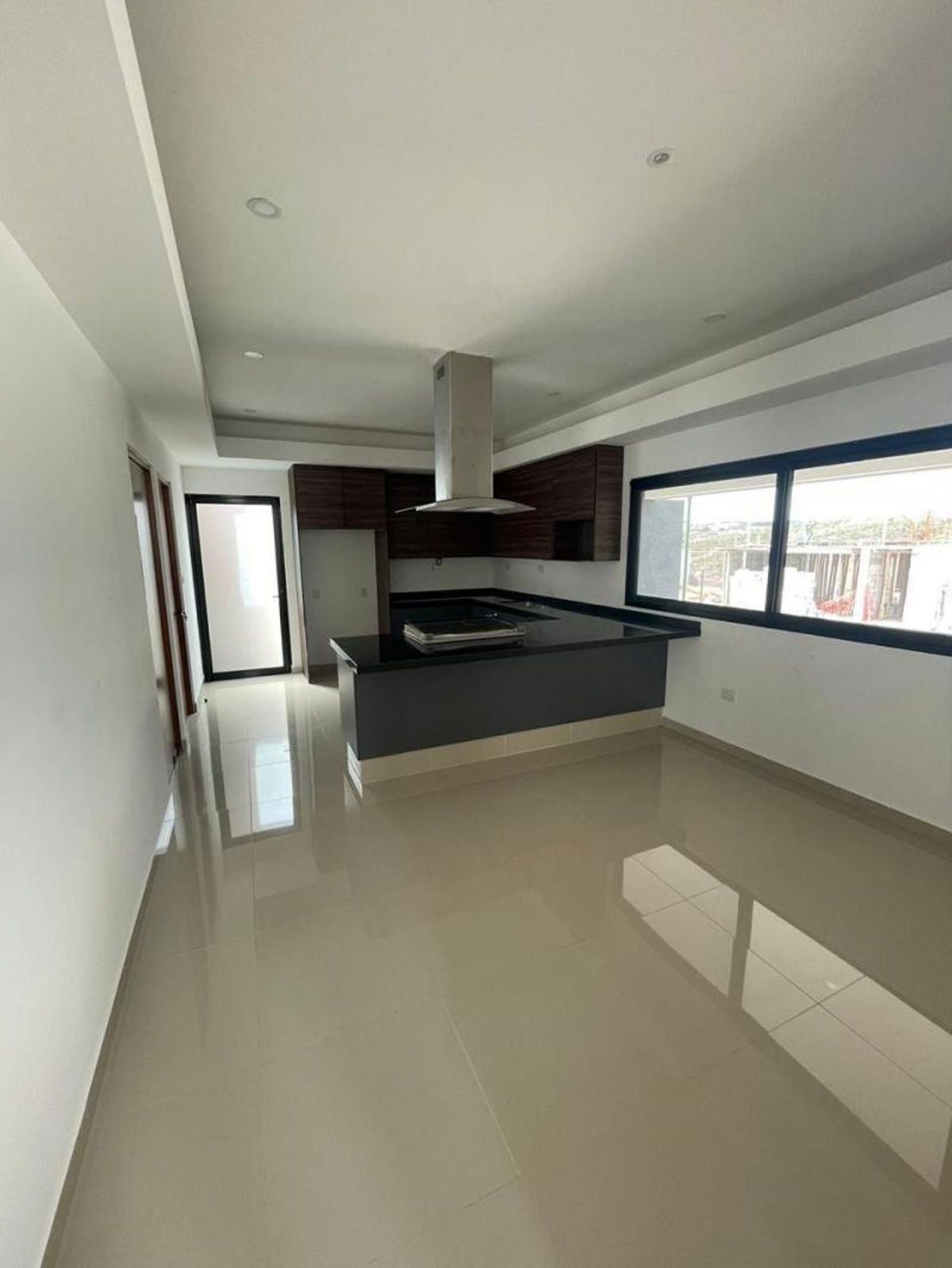 Cocina abierta con isla negra, campana de acero inoxidable, gabinetes oscuros y piso brillante