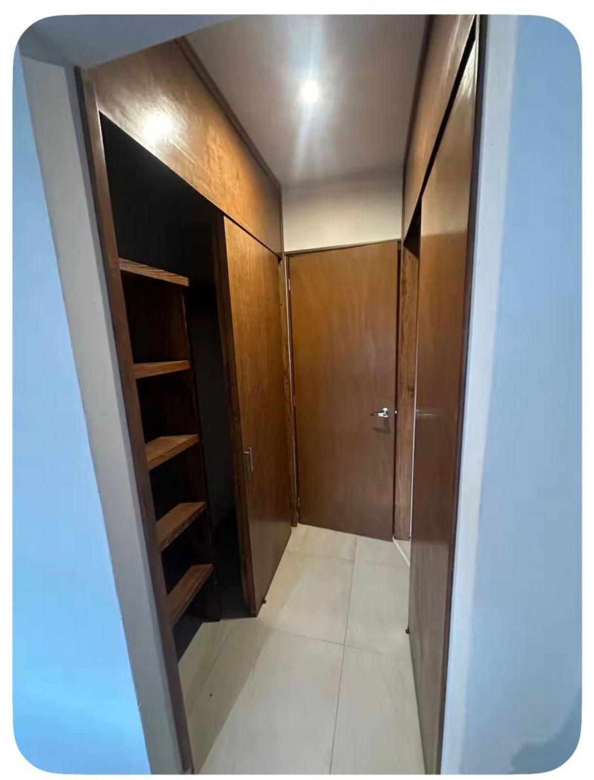 Pasillo con vestidor de madera, repisas, puerta al fondo y piso de loseta clara