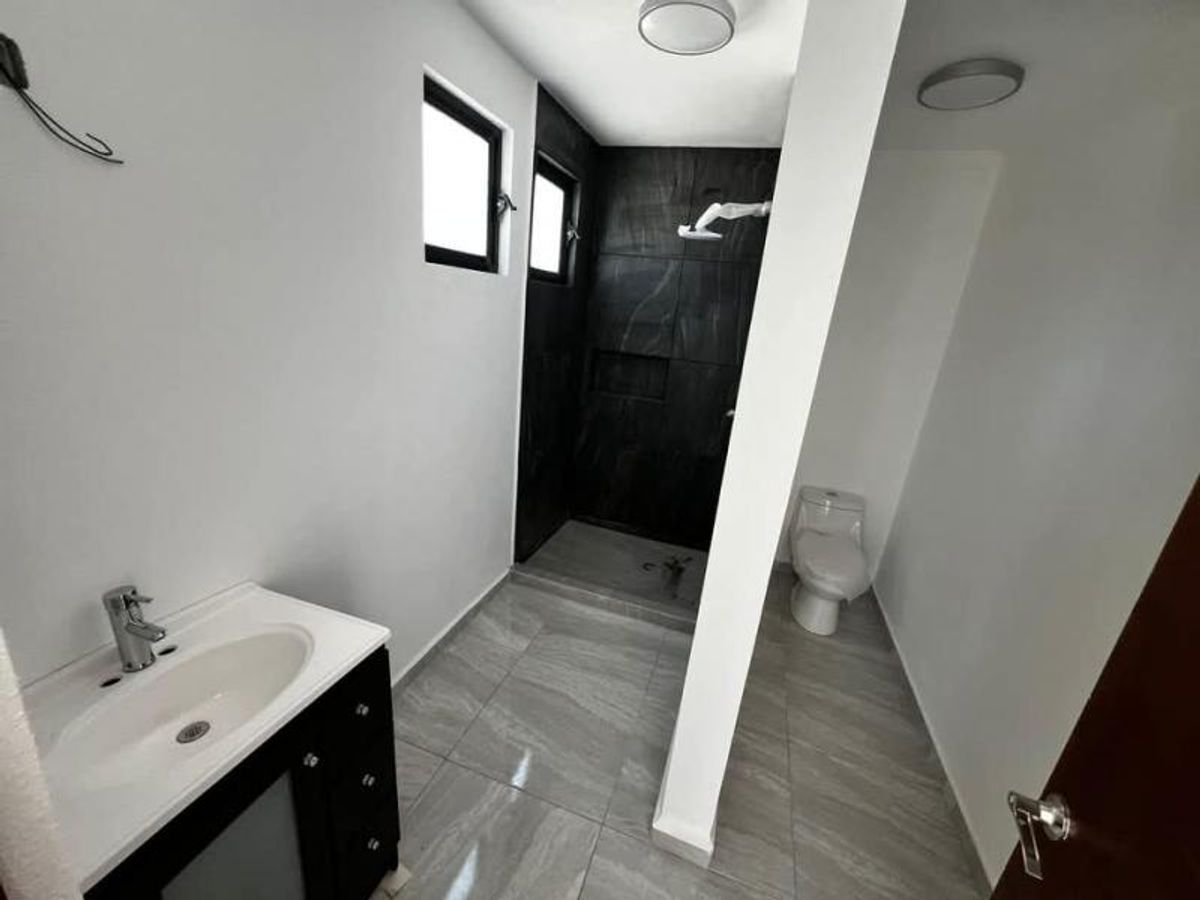 Baño con lavabo sobre mueble negro, piso gris y regadera con azulejos negros