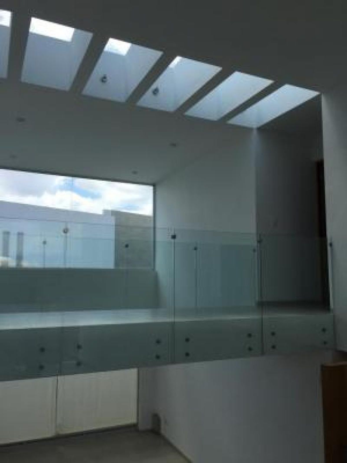 Pasillo en doble altura con barandal de cristal, tragaluces superiores y ventanal exterior