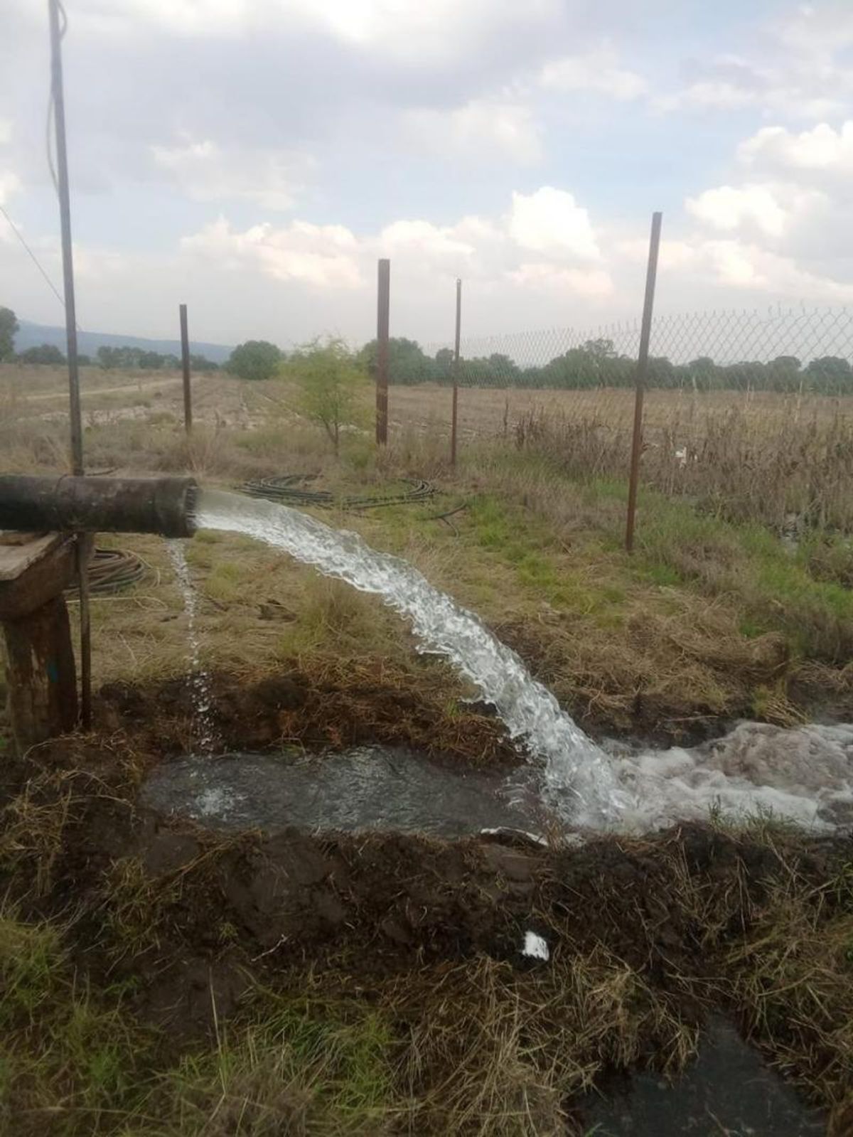 Tubería de riego descargando agua sobre una zanja de tierra en el campo