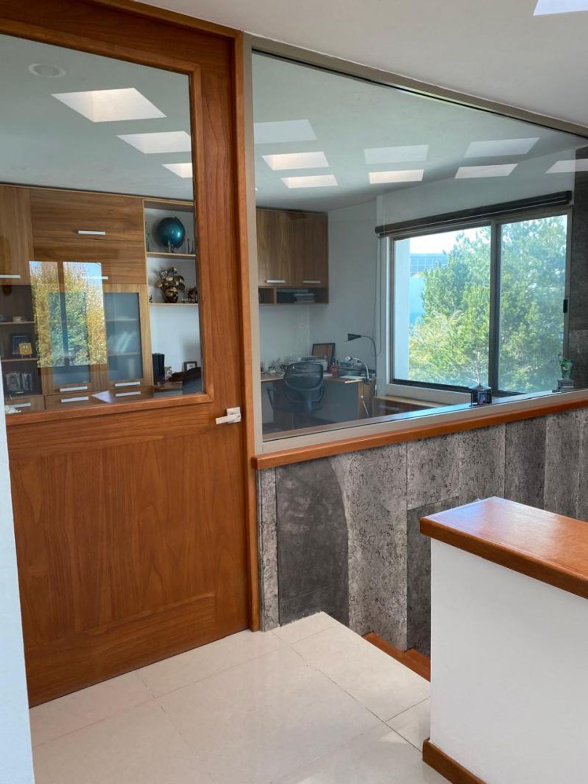 Puerta de madera con cristal, ventanal divisorio, muro de piedra y piso claro