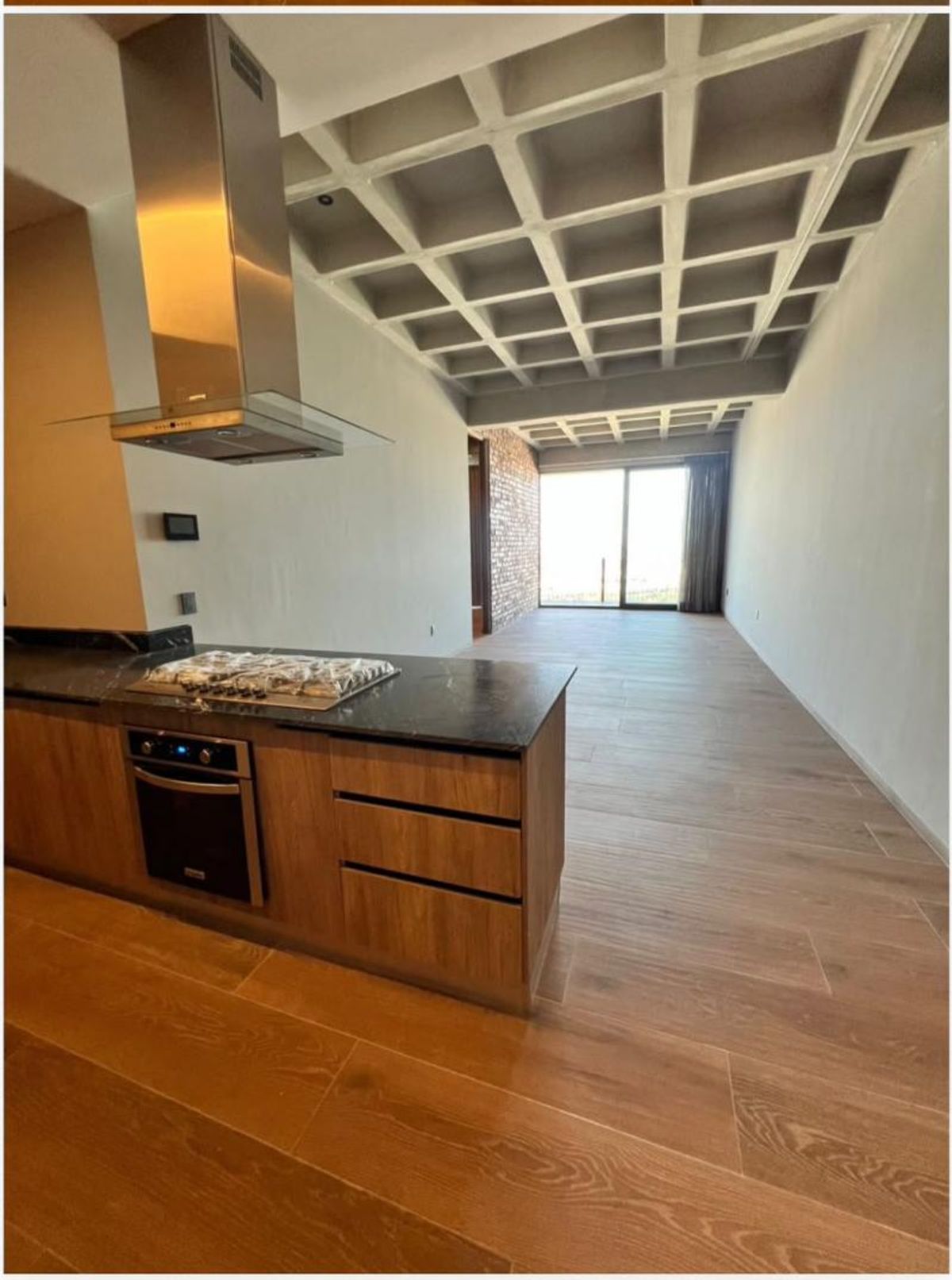 Cocina con isla de madera, estufa, campana de acero y techo reticular de concreto