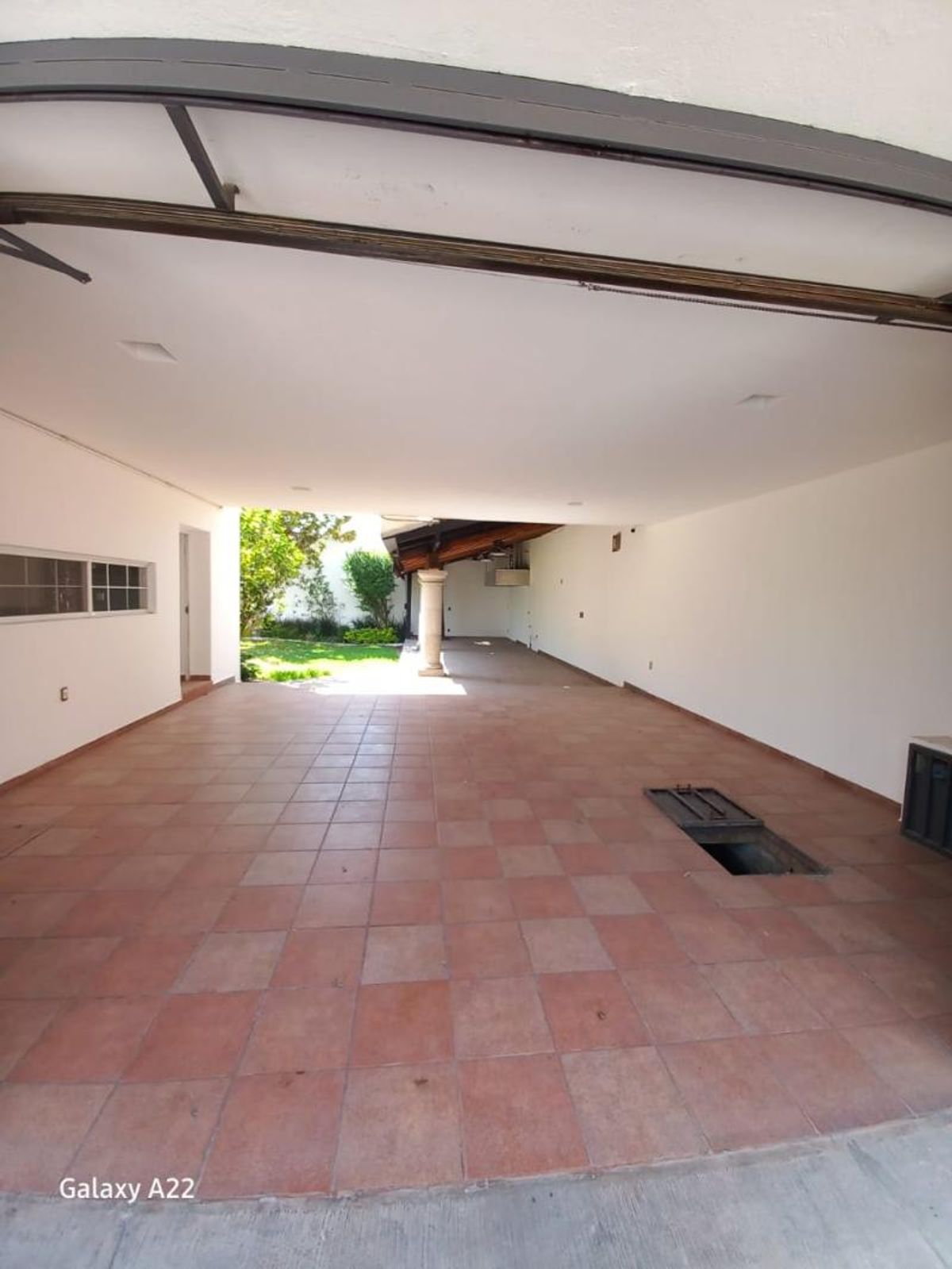 Cochera techada con piso de azulejos terracota, paredes blancas y vista hacia el jardín
