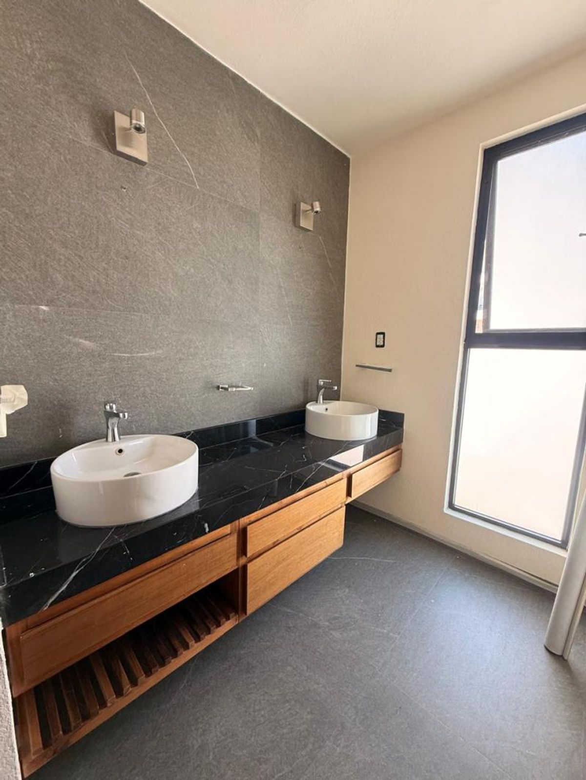 Baño con dos lavabos sobre encimera negra, mueble de madera y pared gris