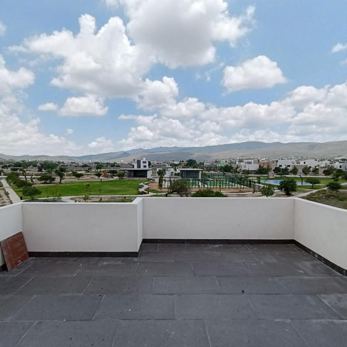 Terraza con piso de loseta gris, muro blanco y vista a parque y montañas