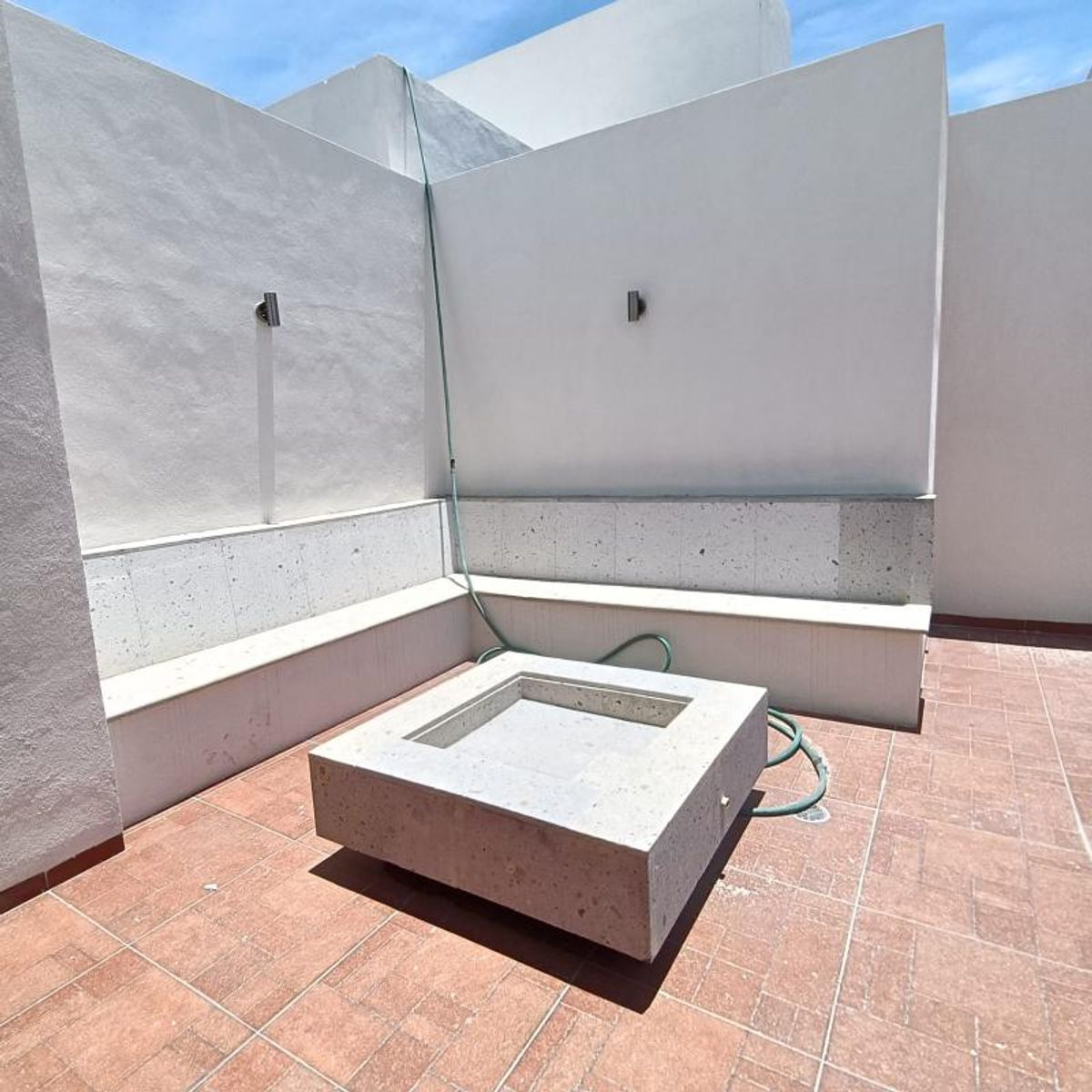 Terraza con piso terracota, muros blancos, banca perimetral de piedra y fogatero central