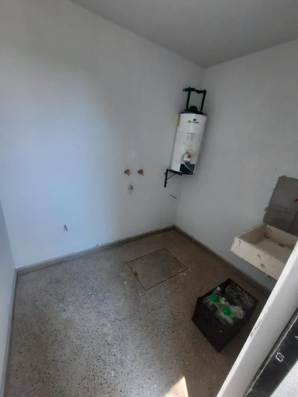 Cuarto de lavado con paredes blancas, piso de concreto, lavadero y calentador de agua