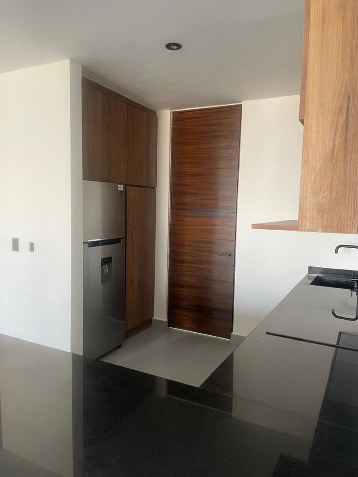 Cocina con cubierta de granito negro, refrigerador de acero inoxidable y gabinetes de madera