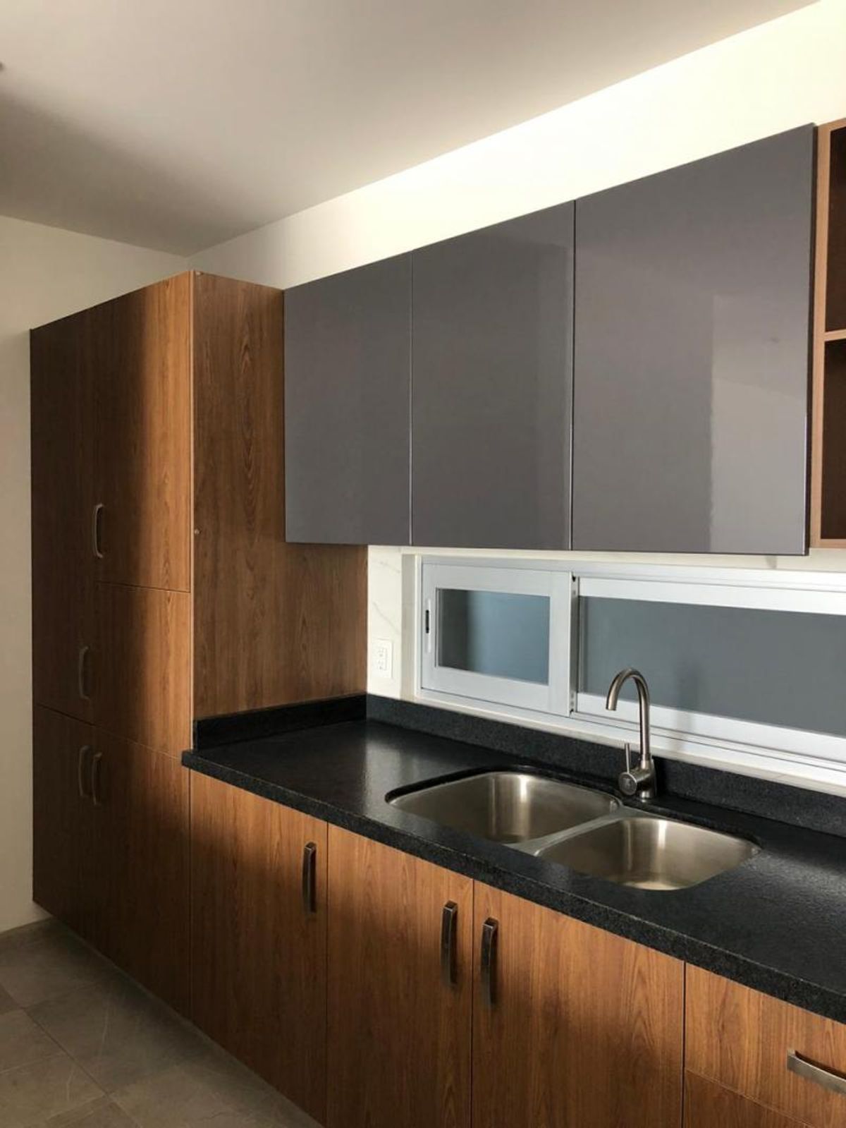 Cocina con cubierta negra, tarja de acero inoxidable y gabinetes de madera y gris