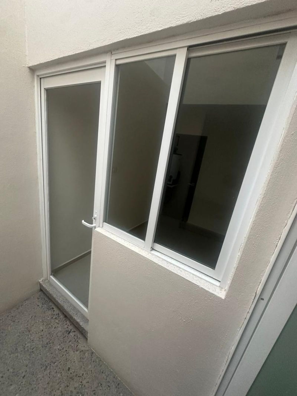 Puerta de vidrio con marco de aluminio blanco junto a ventanal sobre muro claro