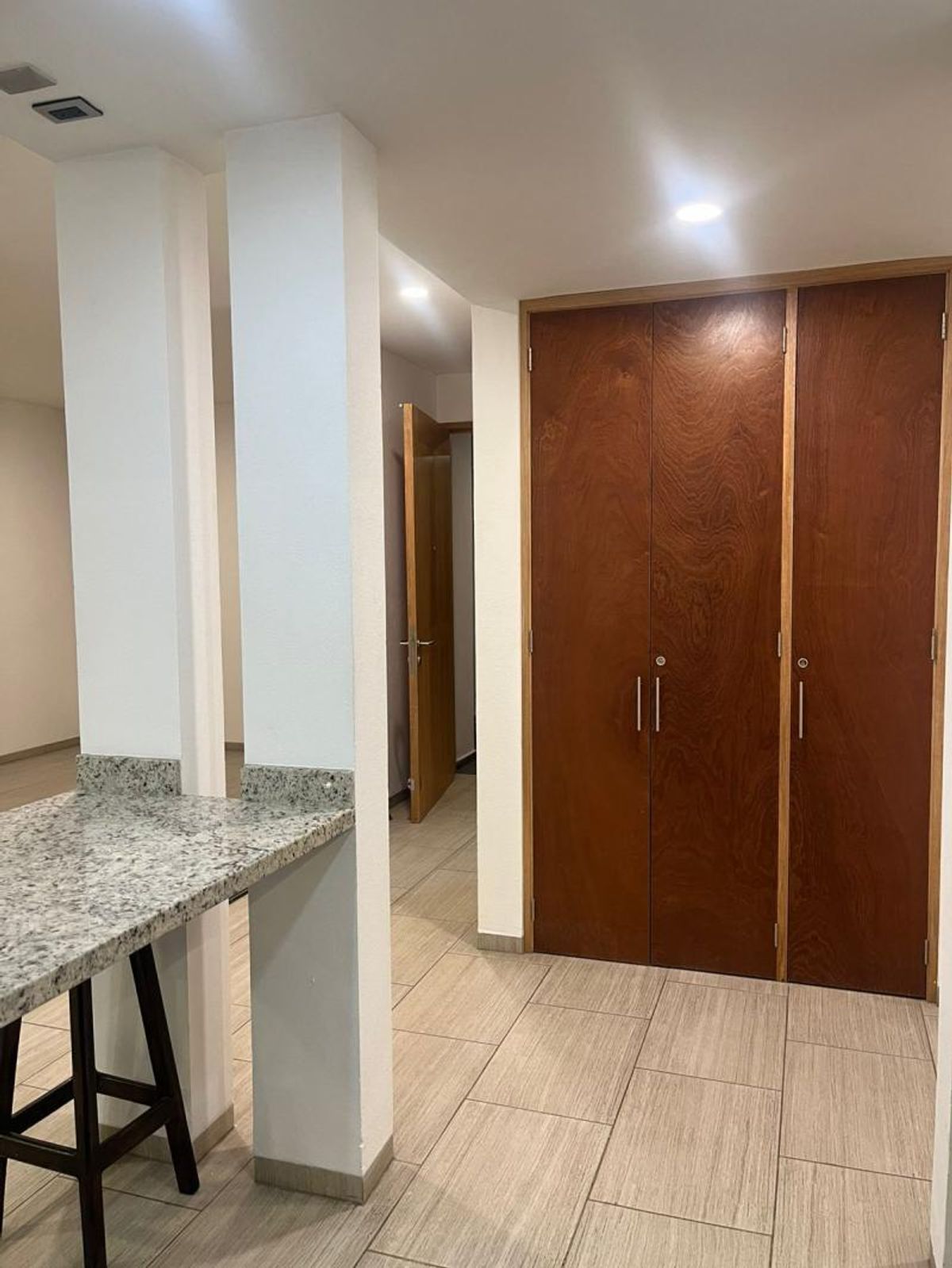 Barra de granito con taburete, clósets de madera y piso de loseta beige