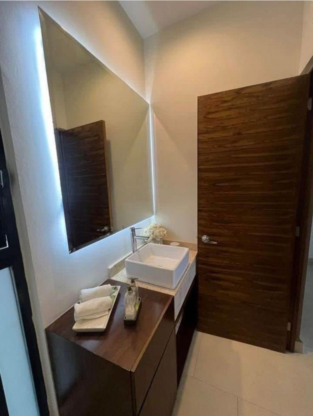 Mueble de baño de madera con lavabo rectangular blanco, espejo retroiluminado y puerta