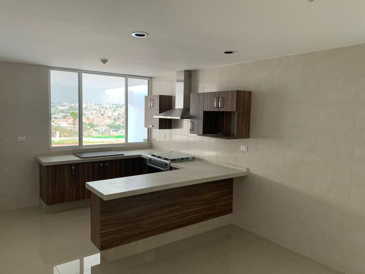 Cocina integral con barra desayunadora, gabinetes de madera, estufa con campana de acero y ventanal