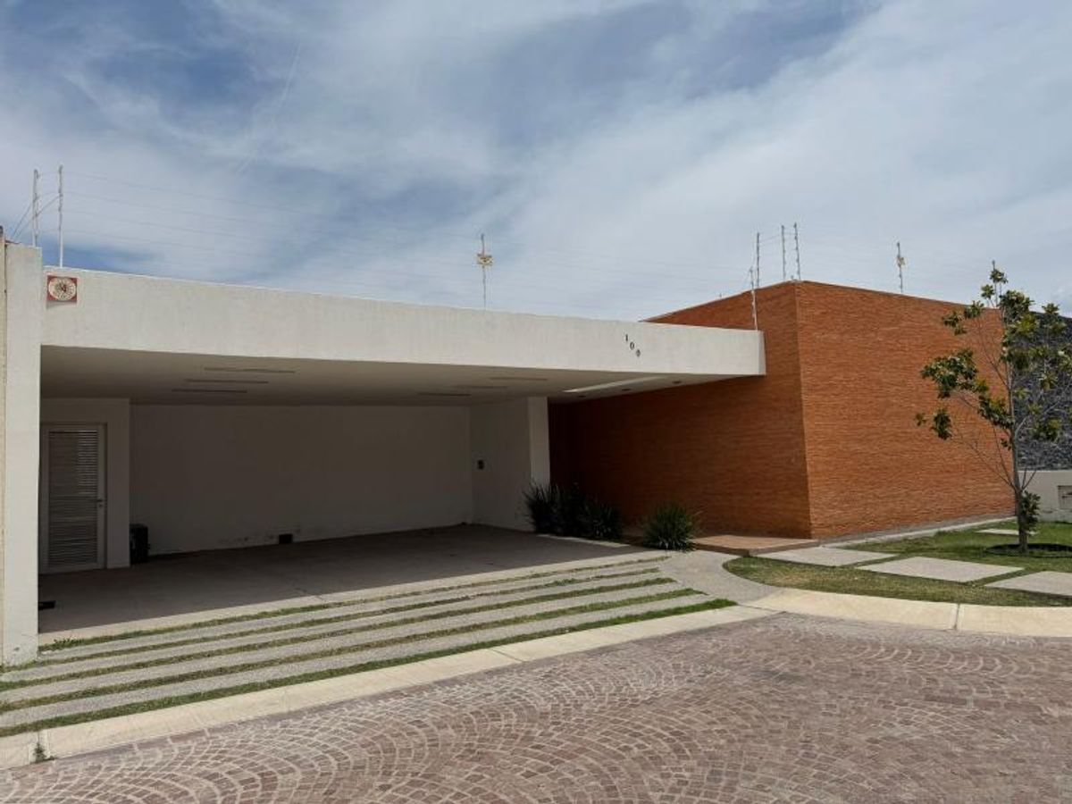 Fachada moderna de una planta con cochera techada blanca y muro de ladrillo anaranjado