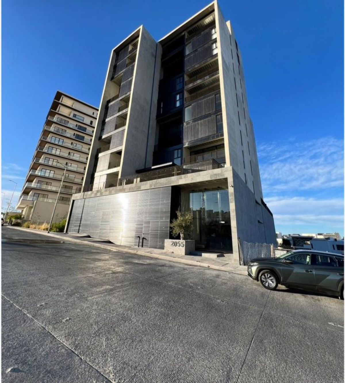 Edificio moderno de departamentos con fachada de concreto gris sobre una calle inclinada