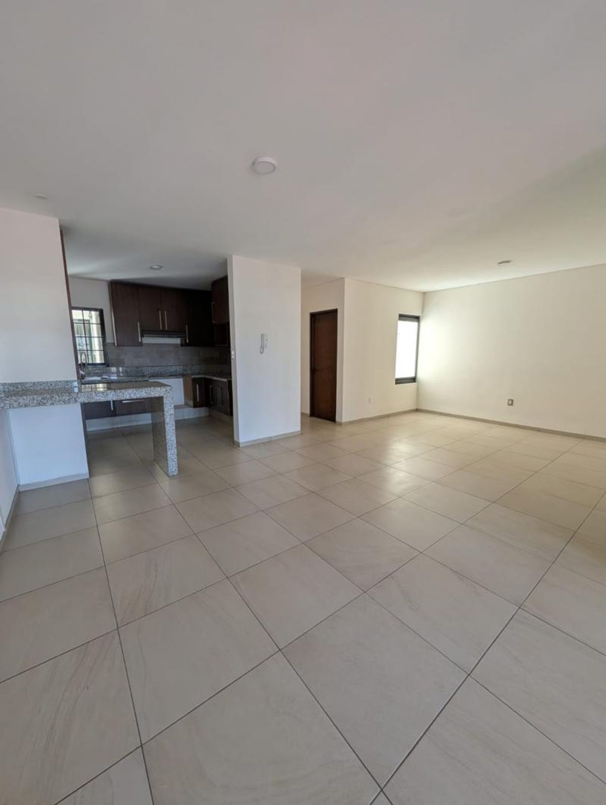 Espacio abierto con piso de loseta clara, cocina integral y barra de granito