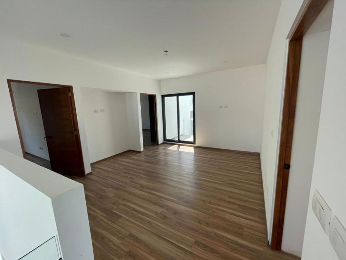 Habitación vacía con piso laminado tipo madera, paredes blancas, puertas oscuras y ventana corrediza