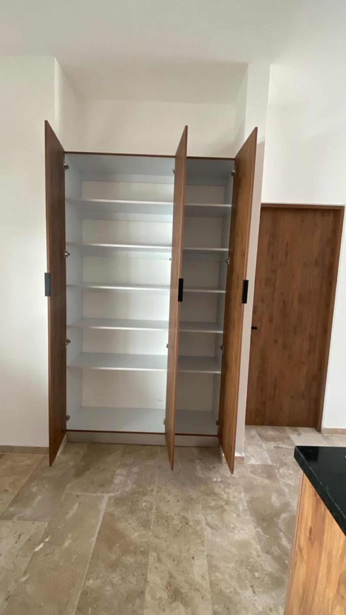 Closet de madera con puertas abiertas, repisas interiores blancas y piso de piedra beige