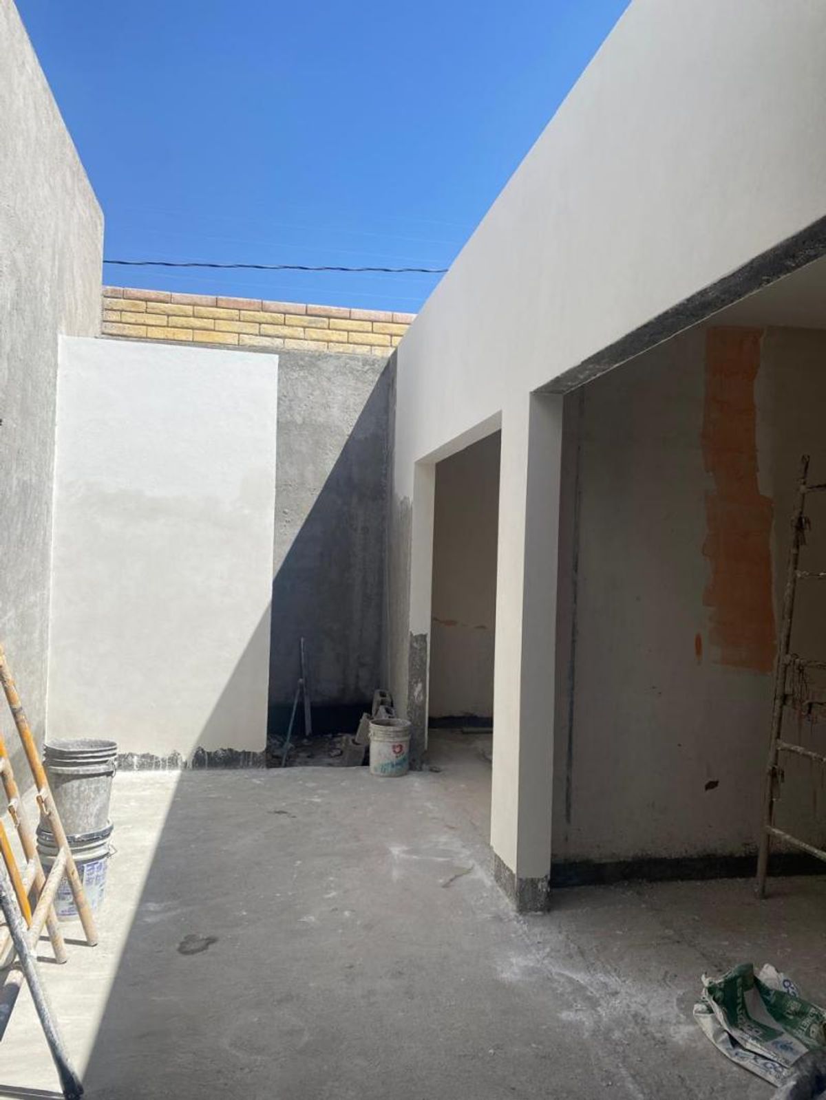 Patio exterior en proceso de construcción con muros de estuco y piso de concreto