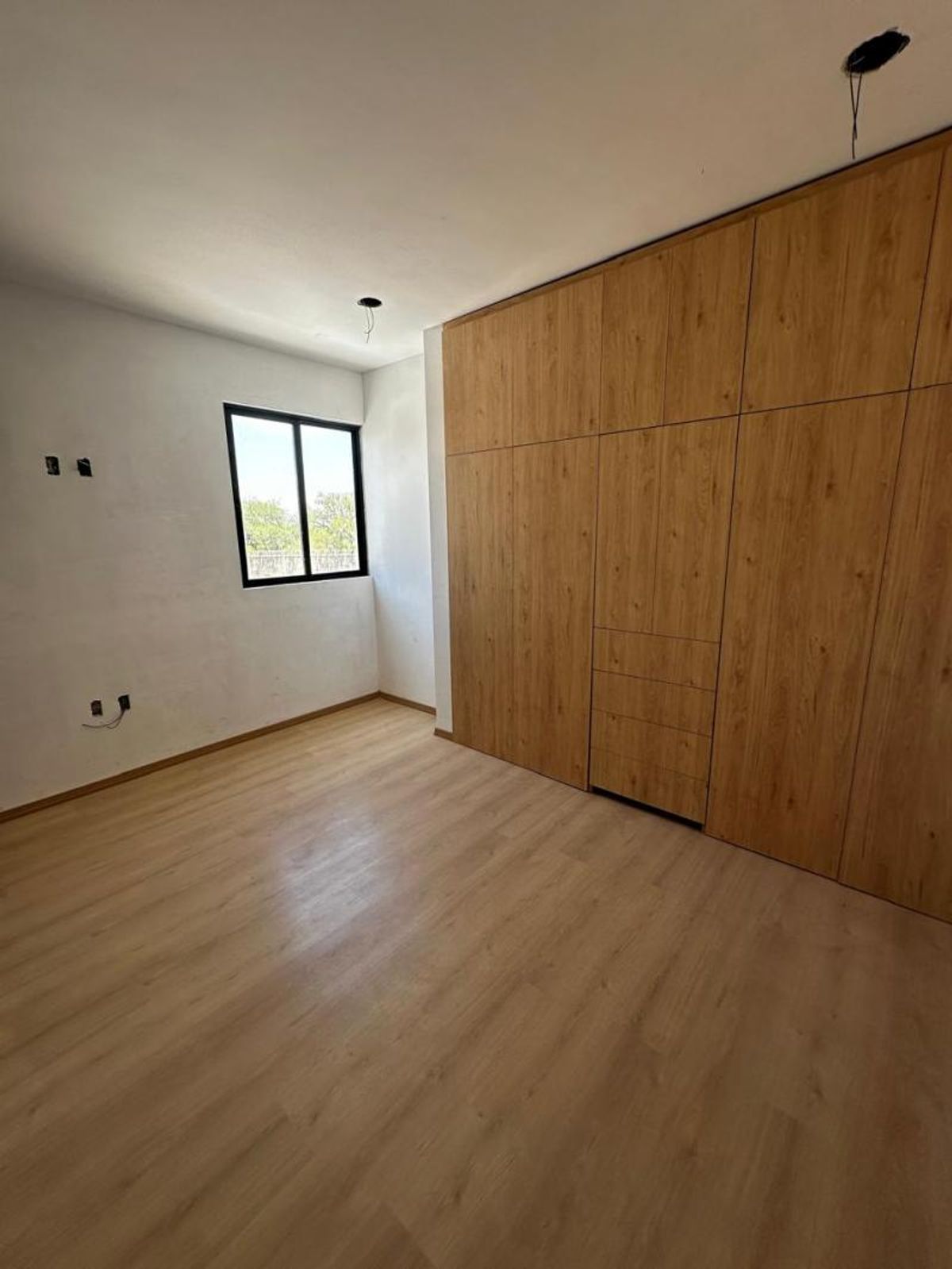 Recámara vacía con piso laminado de madera, clóset empotrado y ventana con marco negro