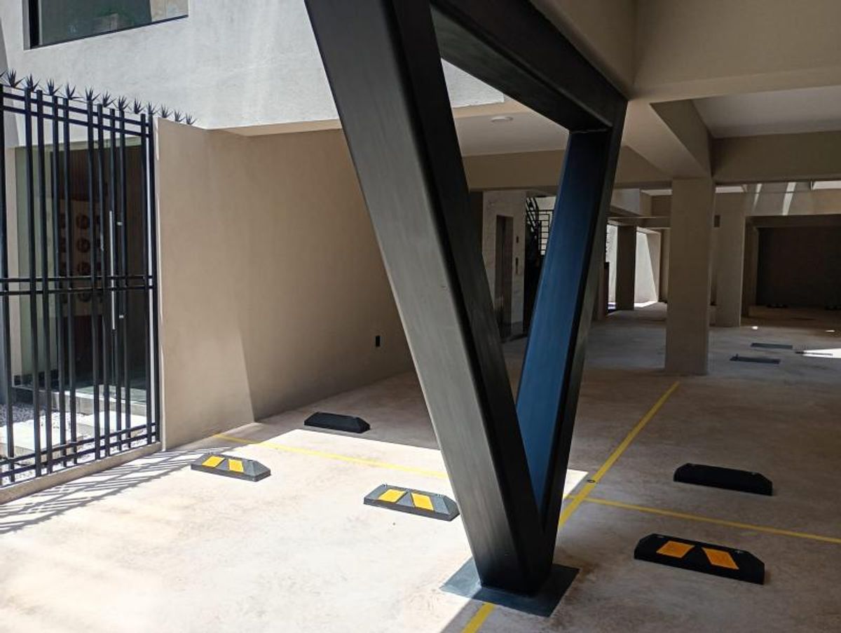 Estacionamiento techado con columna de acero en V, topes negros y líneas amarillas