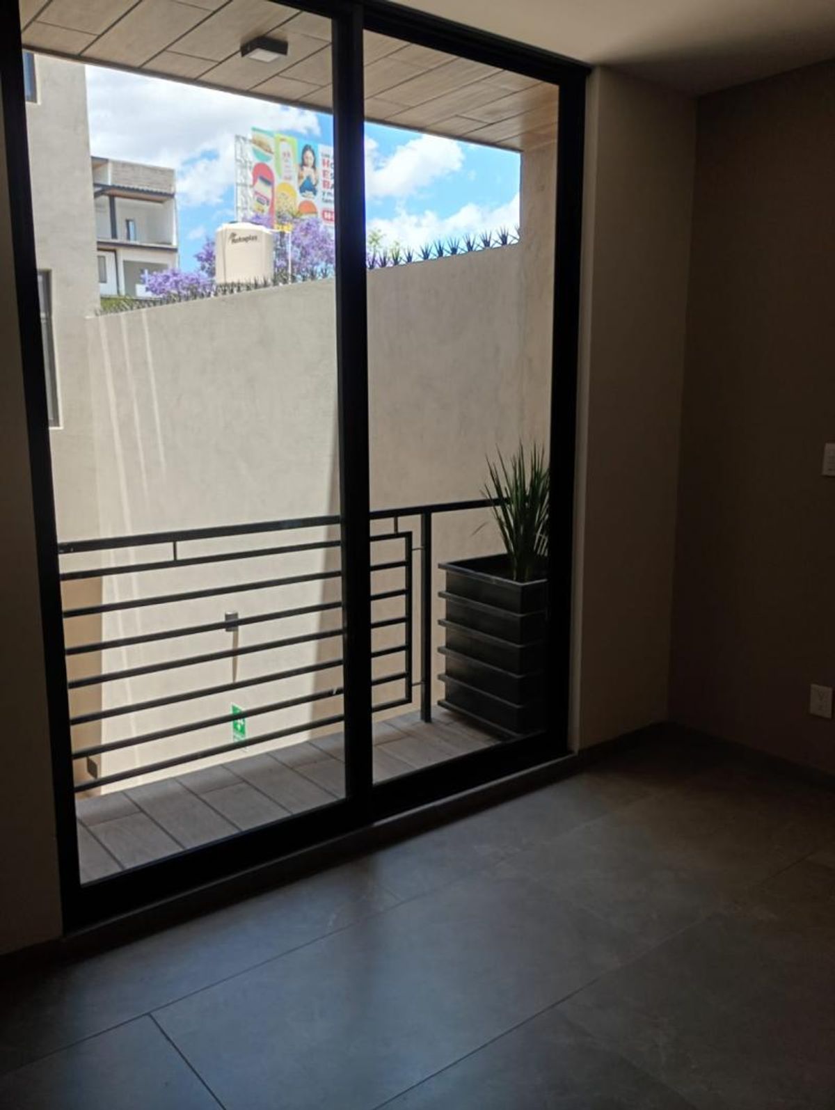 Interior con piso gris y ventanal corredizo hacia un balcón con barandal de metal