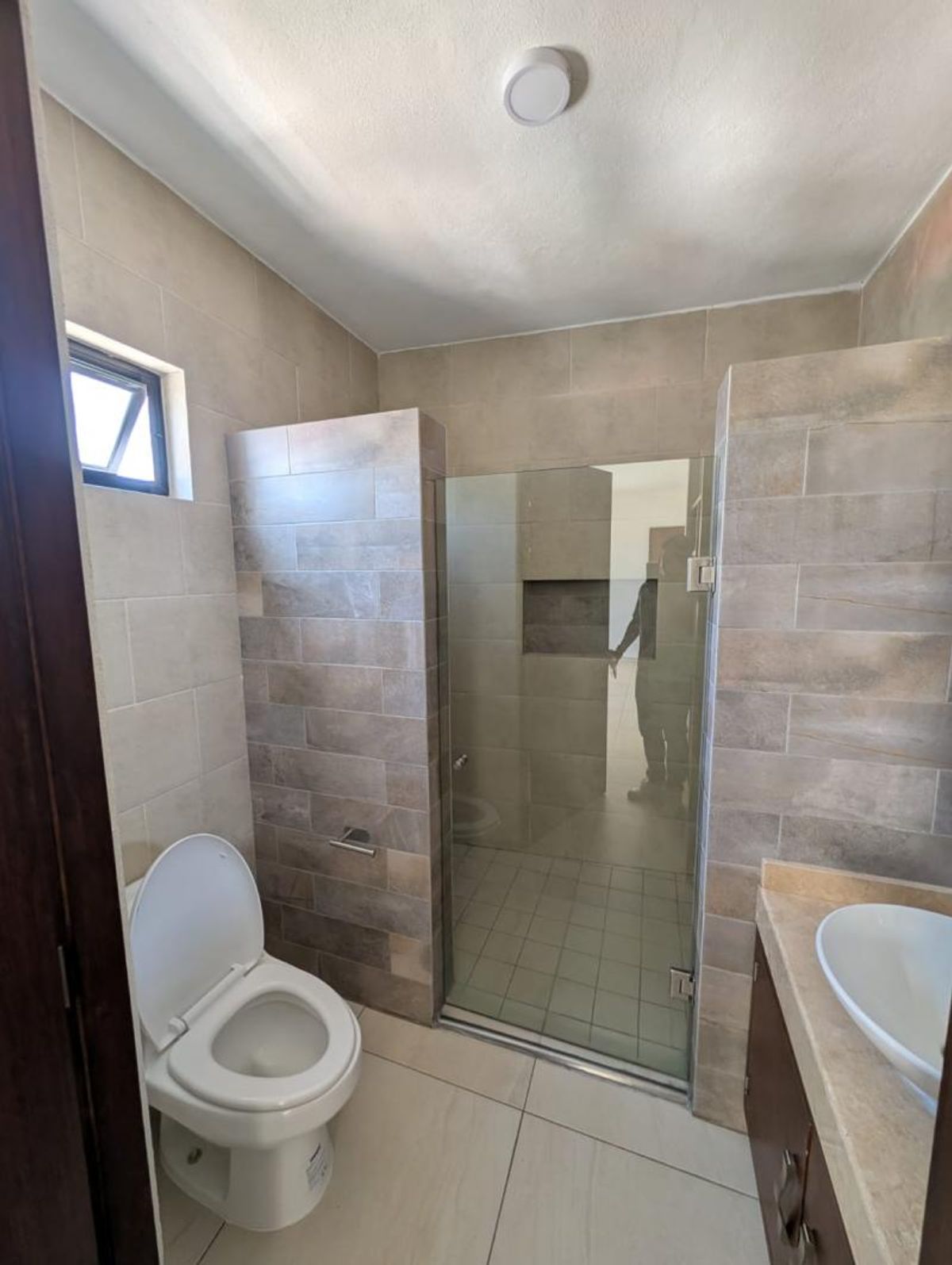 Baño con inodoro blanco, regadera con cancel de cristal y muros revestidos de azulejo
