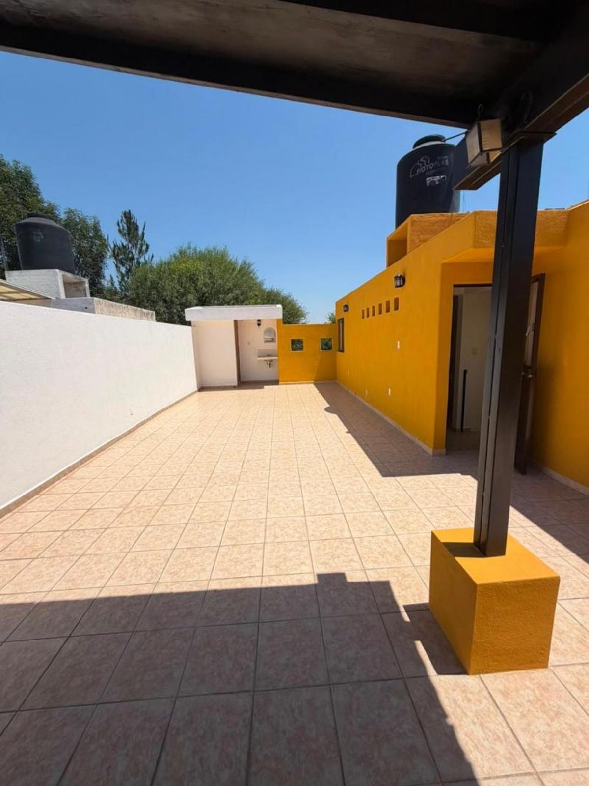 Terraza al aire libre con piso de azulejo beige, muros amarillos y barda blanca