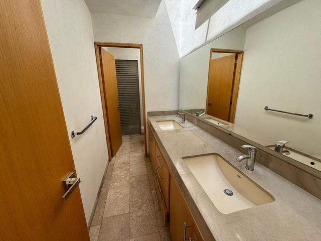 Baño con lavabo doble, cubierta de piedra beige, gabinetes de madera y espejo amplio