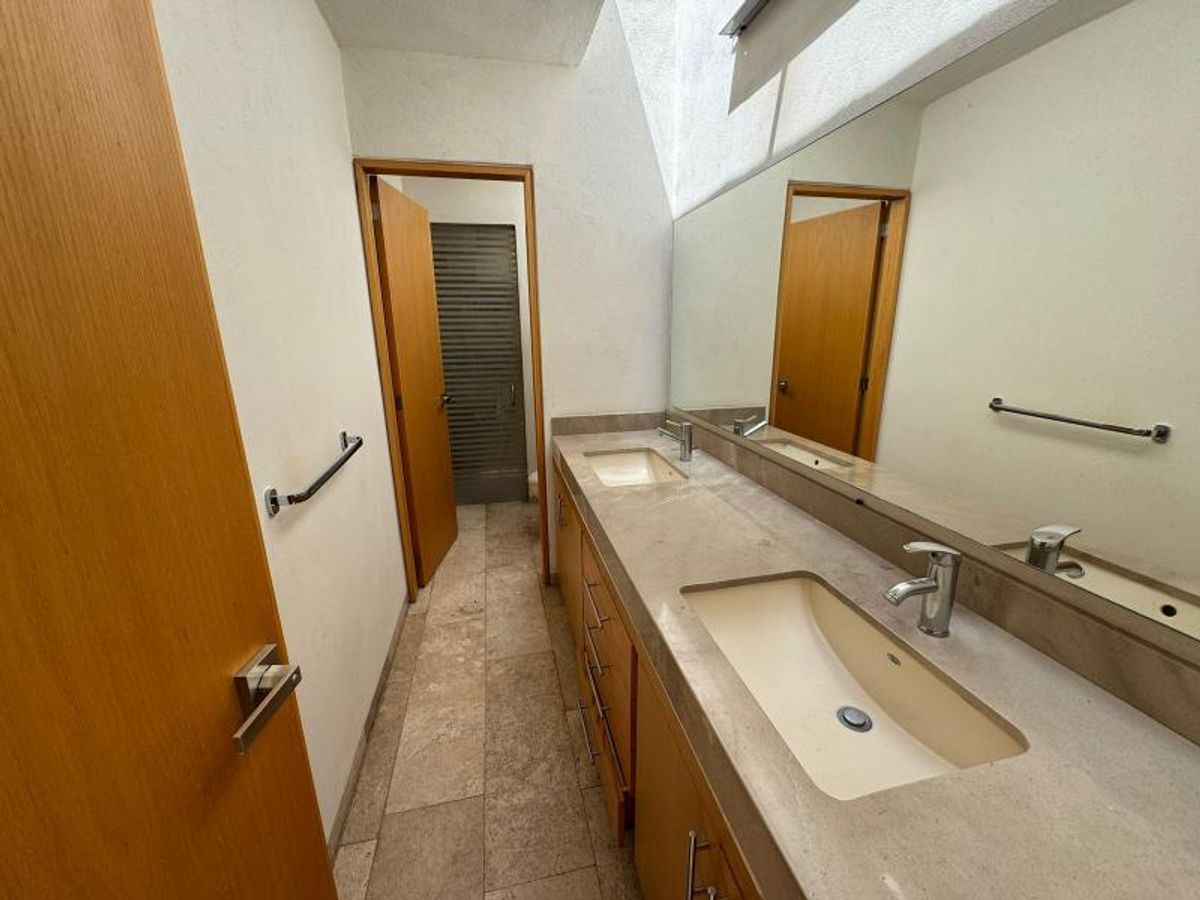 Baño con lavabo doble, cubierta de piedra beige, gabinetes de madera y espejo amplio