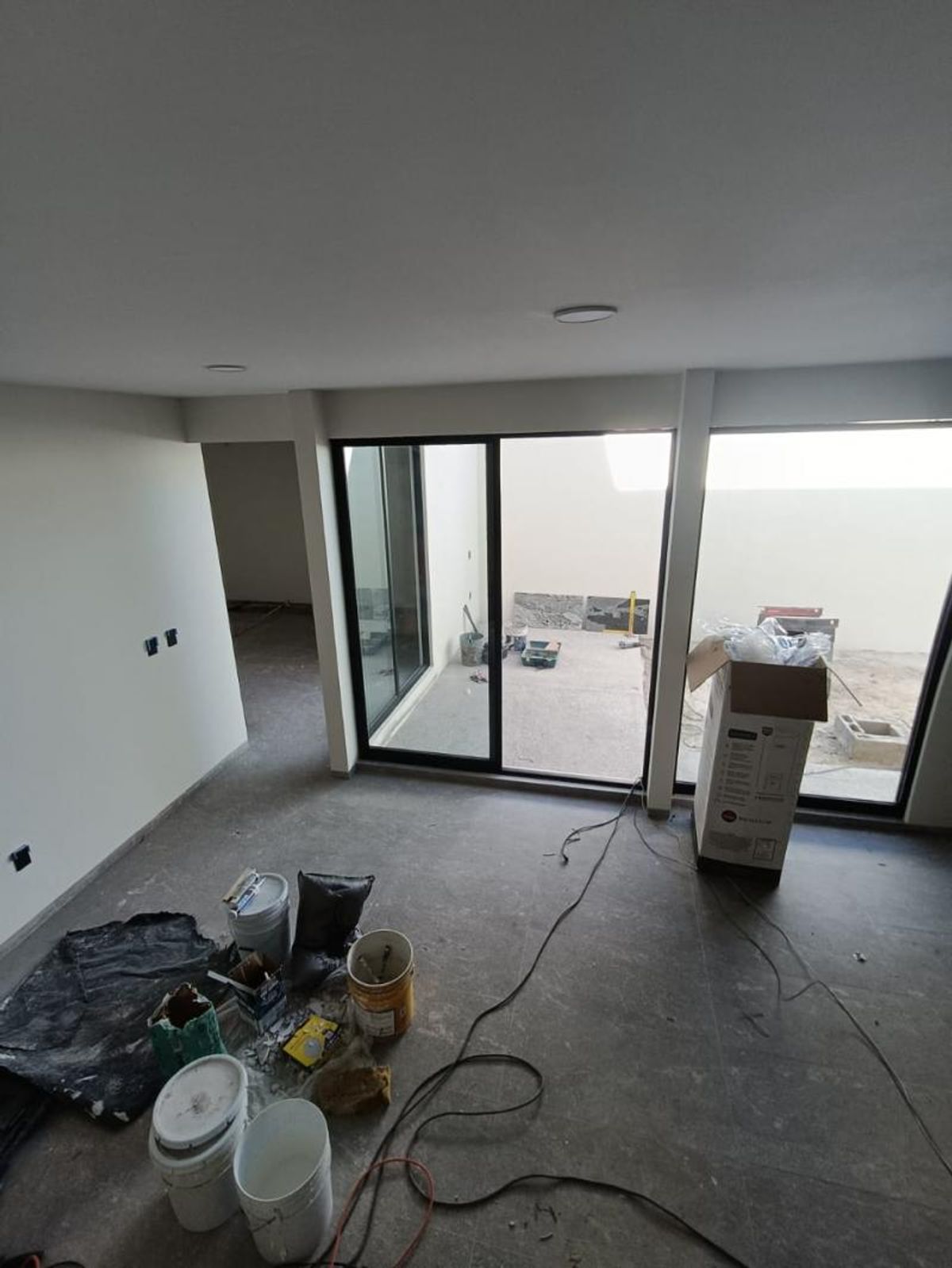 Habitación interior en construcción con ventanales de marco negro, piso gris y luces empotradas en el techo