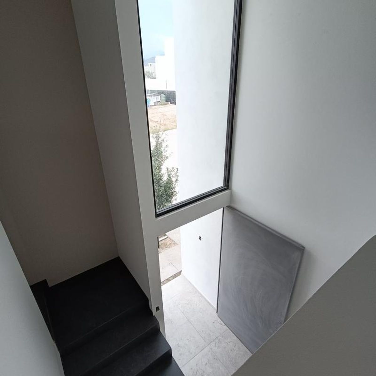 Escalera interior negra, paredes de color blanco y ventanal vertical con vista exterior