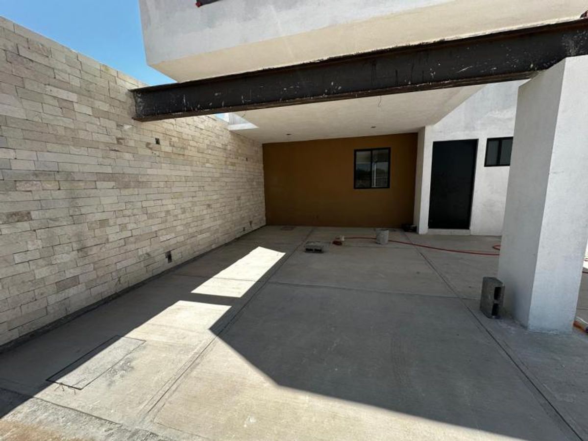 Cochera techada con piso de concreto, viga de acero expuesta y muro de piedra