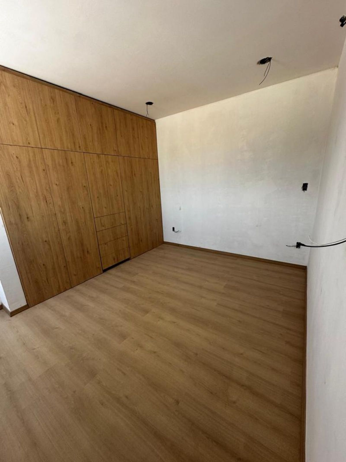Recámara vacía con closet de madera integrado, piso laminado claro y paredes blancas