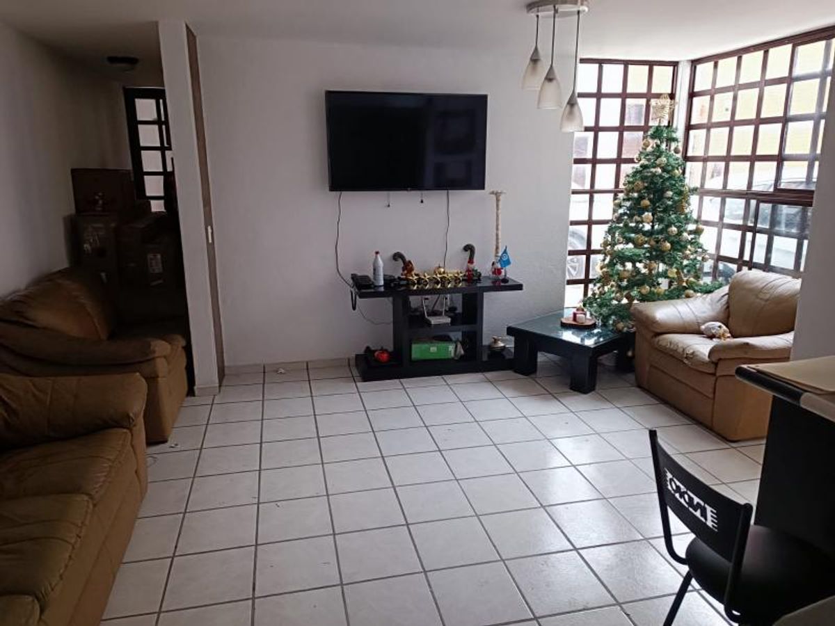 Sala con piso de azulejo claro, sillones de piel café y televisión montada