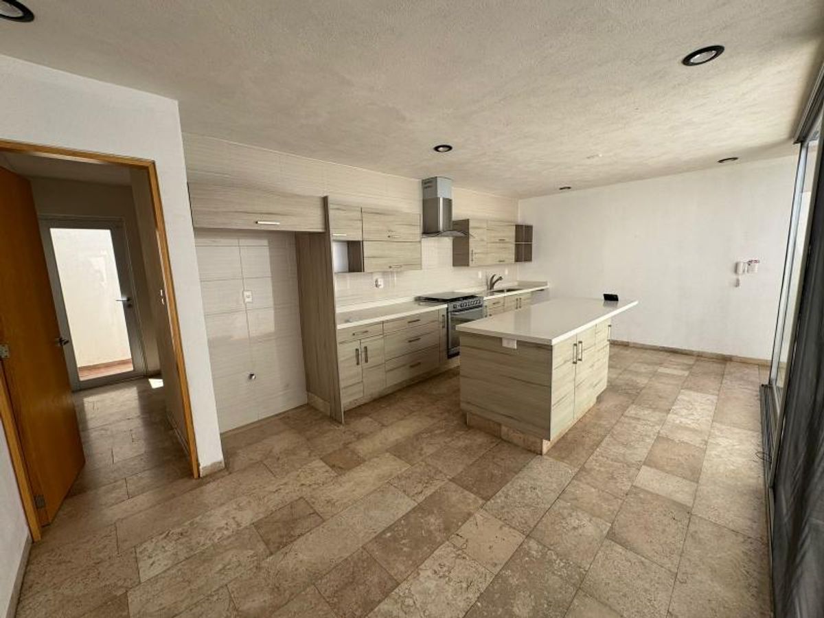 Cocina con isla central, gabinetes de madera clara, campana de acero y piso beige