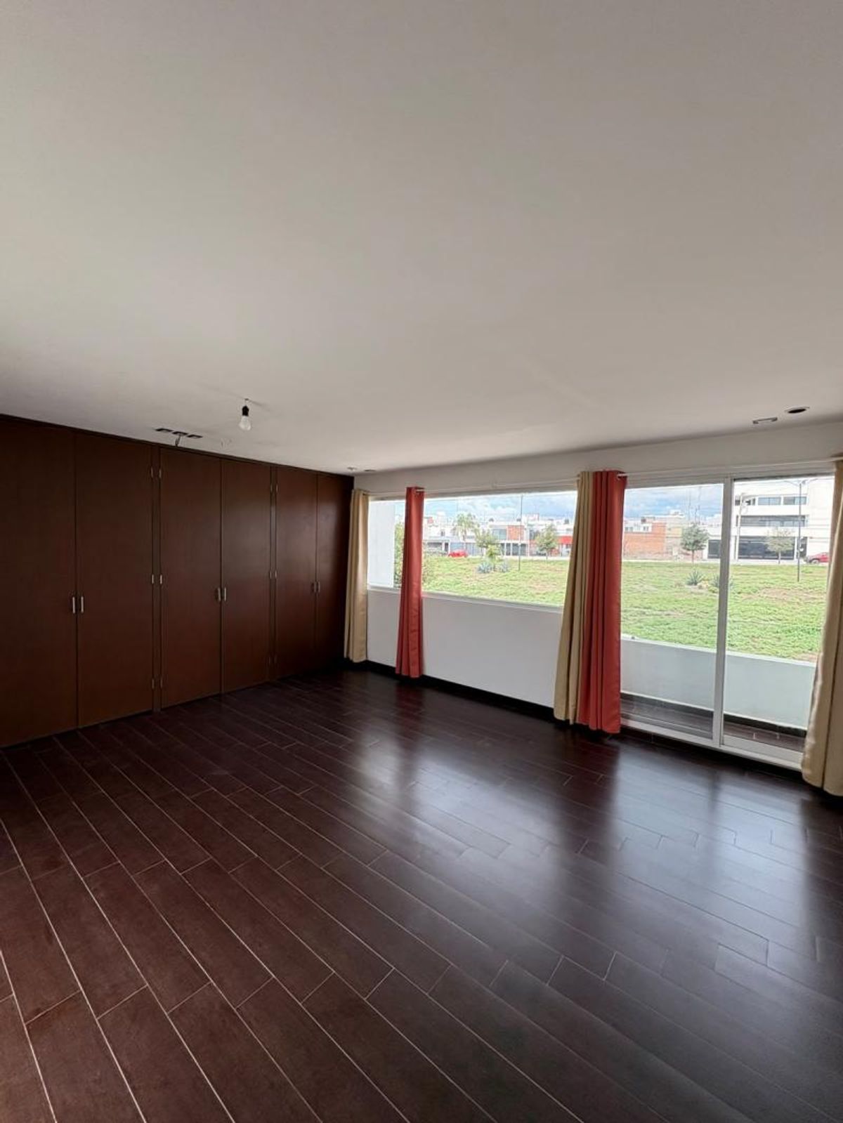 Habitación con piso de madera oscura, clóset empotrado y ventanal con vista a área verde