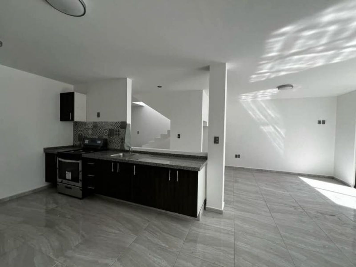 Cocina abierta con gabinetes oscuros, cubierta gris, estufa integrada y piso cerámico claro